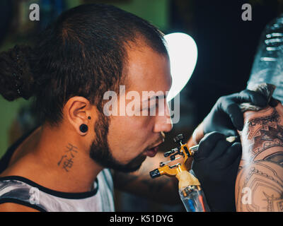 Portrait of man tattoo master with dreadlocks showing process of creation tattoo on female body under the lamp light.Professional artist working in sa Stock Photo