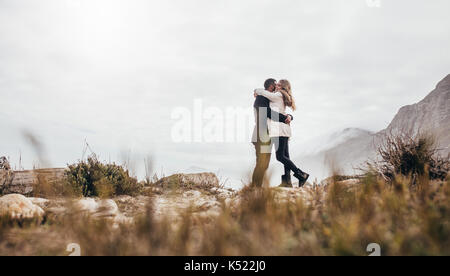 Beautiful couple in winter clothes embracing at the beach. Romantic young couple on winter beach vacation. Stock Photo