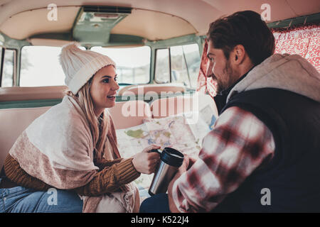 Two friends on a road trip sitting inside the van talking and having coffee. Young man and woman travelling in the camper van. Stock Photo