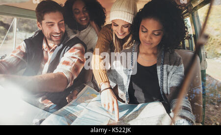 Friends on roadtrip reading map for directions. Group of man and women travelling together in van. Stock Photo