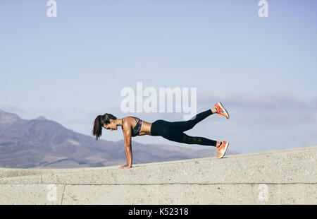 Young muscular woman doing core exercise outdoors. Fit female doing press-ups during training session. Side view shot. Stock Photo
