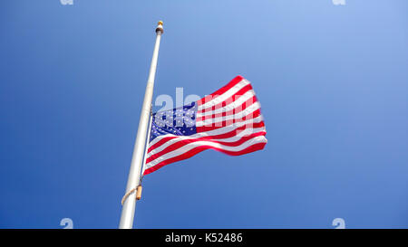 American flag flying at half mast aka half staff against a clear blue sky Stock Photo