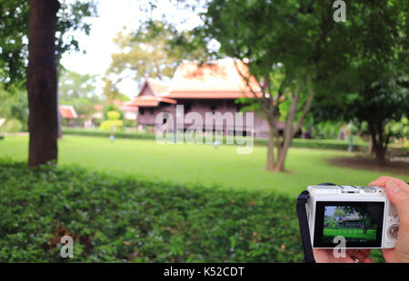 Woman'hand holding a camera for taking picture of an impressive Thai style traditional vintage house, Nakhon Pathom, Thailand Stock Photo