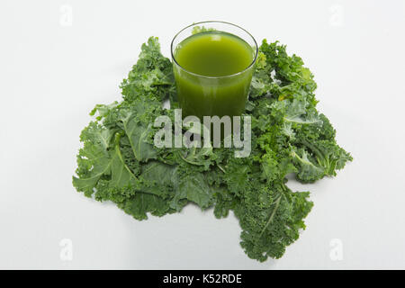 High angle view of juice amidst kale leaves on white background Stock Photo