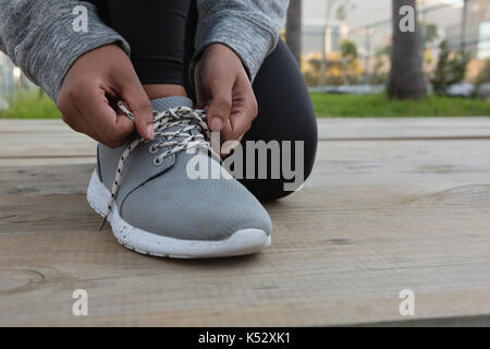 Low section of female athlete tying shoelace while kneeling on boardwalk Stock Photo