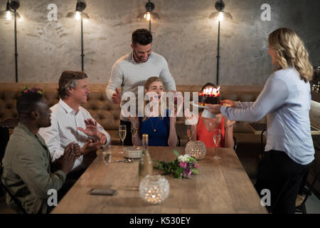 Woman receiving surprise birthday cake from her friends in restaurant Stock Photo