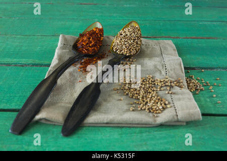 Crushed red pepper and coriander seeds in spoon on wooden table Stock Photo