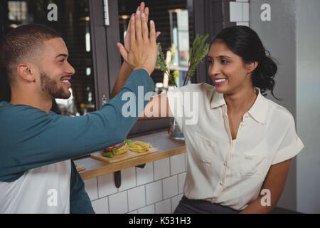 Happy young couple giving high-five while sitting in cafe Stock Photo