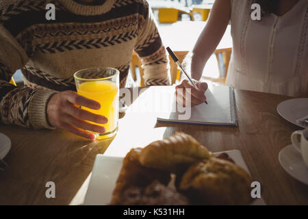 Mid section of woman with man writing on book while sitting at table in cafe Stock Photo