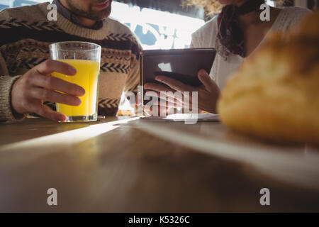 Mid section of woman with man using digital tablet at table in cafe