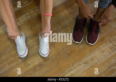 Low section of dancers tying shoelaces on wooden floor at studio Stock Photo