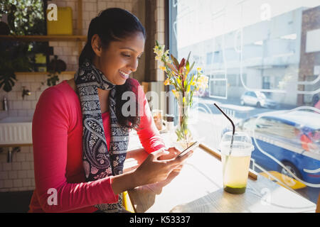 Smiling young woman using phone at window sill in cafe Stock Photo