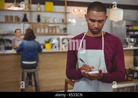 Young owner taking order while standing in cafe Stock Photo