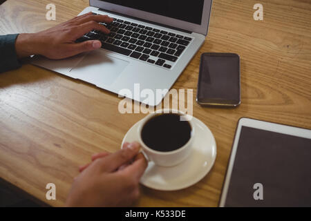 Cropped hands of man having black coffee while using laptop at wooden table in cafe Stock Photo