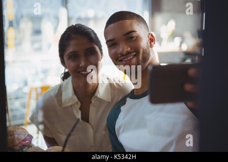 Smiling young man with woman taking selfie seen through glass in cafe Stock Photo