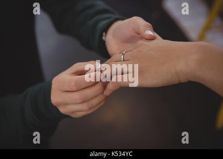 Cropped image of man putting ring on woman finger at cafe Stock Photo