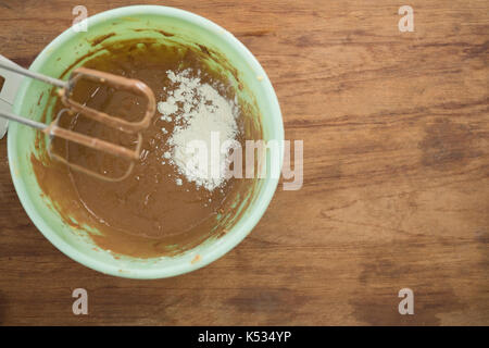 Overhead view of flour with chocolate batter in bowl by electric mixer on wooden table Stock Photo