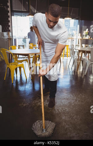 Full length of young waiter mopping floor in cafe Stock Photo