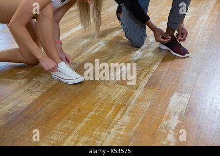 Low section of dancers tying shoelaces on wooden floor in studio Stock Photo