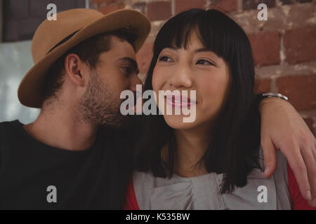 Young man wearing hat whispering in woman ear at cafe