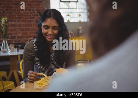 Woman with friend having French fries while sitting on chair in cafe Stock Photo