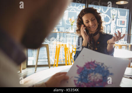 Young woman with man talking on mobile phone at table in cafe Stock Photo