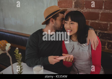 Young man whispering in woman ear while sitting at cafe Stock Photo