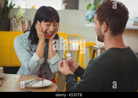 Young man gifting ring to shocked happy woman in cafe Stock Photo