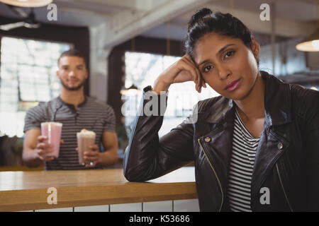 Portrait of relaxed young woman with friend holding milkshake glasses in cafe