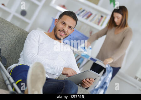 man watching tablet not wanting to clean with his wife Stock Photo