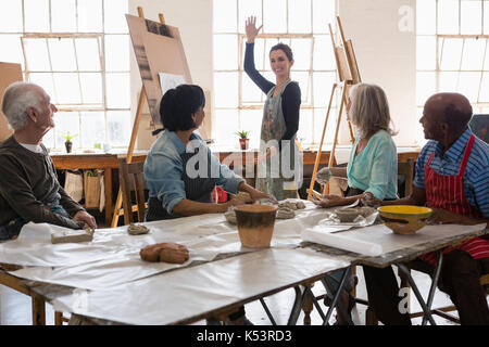 Senior man and woman looking at female instructor gesturing while standing in art class Stock Photo