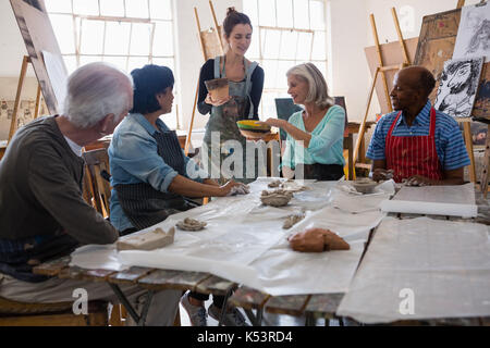 Female instructor showing clay pots to senior people at table in art class Stock Photo
