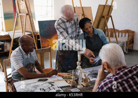 Senior woman discussing over painting with friends in art class Stock Photo