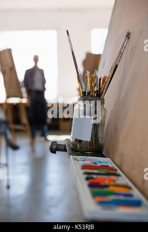 Close up of crayon box and paint brushes in jar on easel in art class Stock Photo