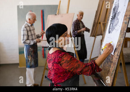 Senior man and woman painting while standing in art class Stock Photo