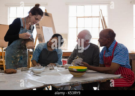 female teacher showing clay pot to senior people in art class Stock Photo