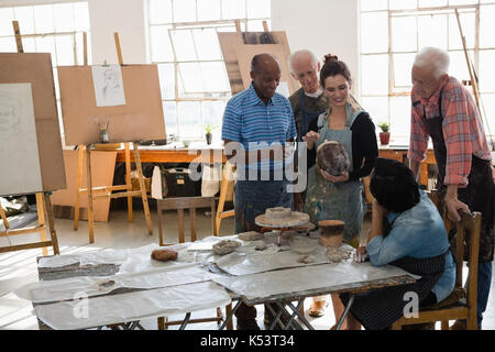 Female instructor holding sculpture while explaining senior people at table in art class Stock Photo