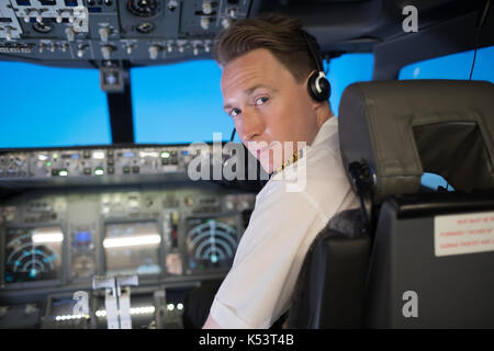 Portrait of handsome young male pilot wearing headphones while sitting on seat in airplane cockpit Stock Photo