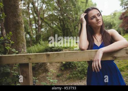 Thoughtful woman leaning on wooden fence in forest Stock Photo