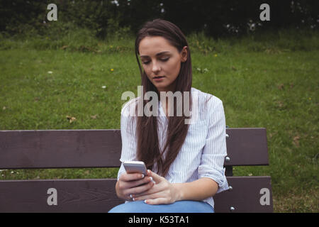 Beautiful woman sitting on bench and using mobile phone in forest Stock Photo