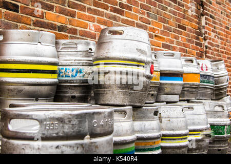 Stacked empty used aluminium beer kegs standing against a brick wall, two stacks high and two stacks deep Stock Photo