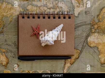 travel flat lay with notepad seashells seastar and black pen placed on world map Stock Photo