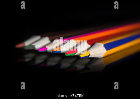 Color pencils on a black mirror. Pencils with double color. black isolated background. Stock Photo