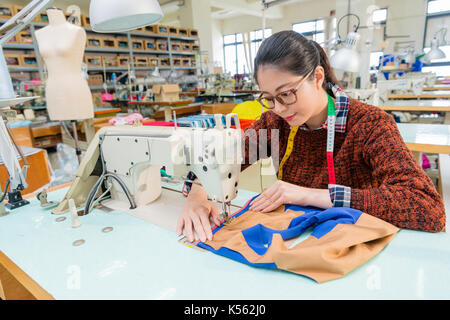 pretty professional female sewing worker using tailor machine making designer new product in fashion studio. Stock Photo