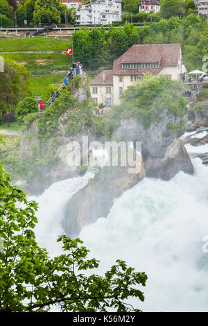 The Rhine Falls vertical landscape. Touristic viewpoint with flag on the rock in fast flowing river water Stock Photo