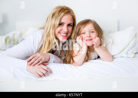 Cute little girl and her mother lying on a bed Stock Photo