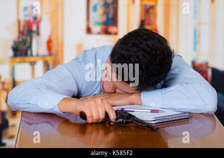 Man with pistol gun laying on a wooden table, wants to commit suicide, inside a house room, room background Stock Photo