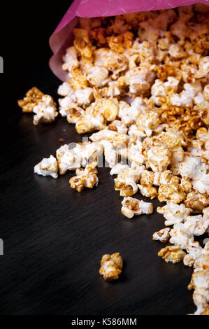 Scattered popcorn on the dark wooden background with couple 3d glasses. Bright movie topic. Fast food. pink paper box. Watching cinema. Stock Photo