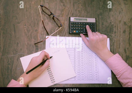 Great concept of finance, woman hand working, calculating, tables, financial calculator, writing on notepad. Stock Photo