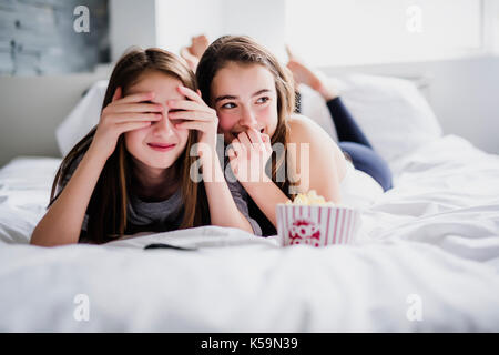 teenage girls eating popcorn and watching horror movie on tv at home Stock Photo
